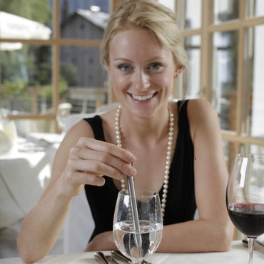 Woman sitting at a table with a glass of water and a glass of red wine, smiling.