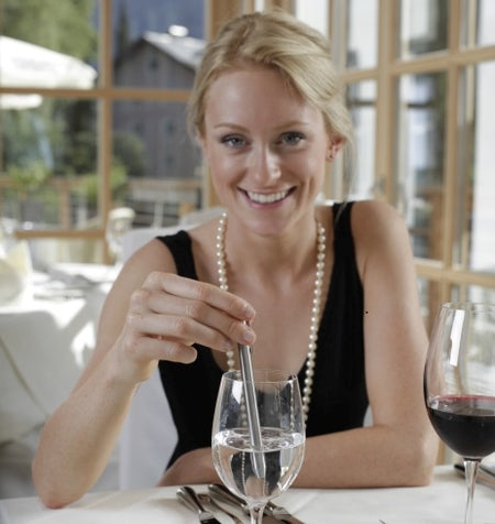 Woman sitting at a table with a glass of water and a glass of red wine, smiling.