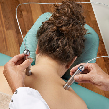 Person receiving a neck and shoulder treatment with electronic devices.