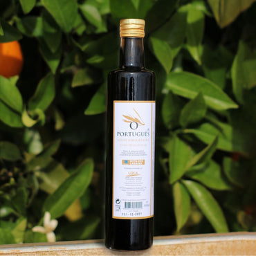 Bottle of Portugues olive oil with a gold cap on a wooden surface with green foliage in the background