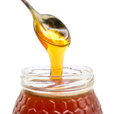 Honey being drizzled from a spoon into a jar on a white background