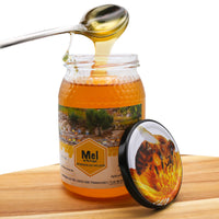 Jar of honey with a spoon dripping honey, on a wooden surface.