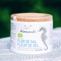 Jar of Flor de Sal with belamandil branding on a textured surface with green blurred background
